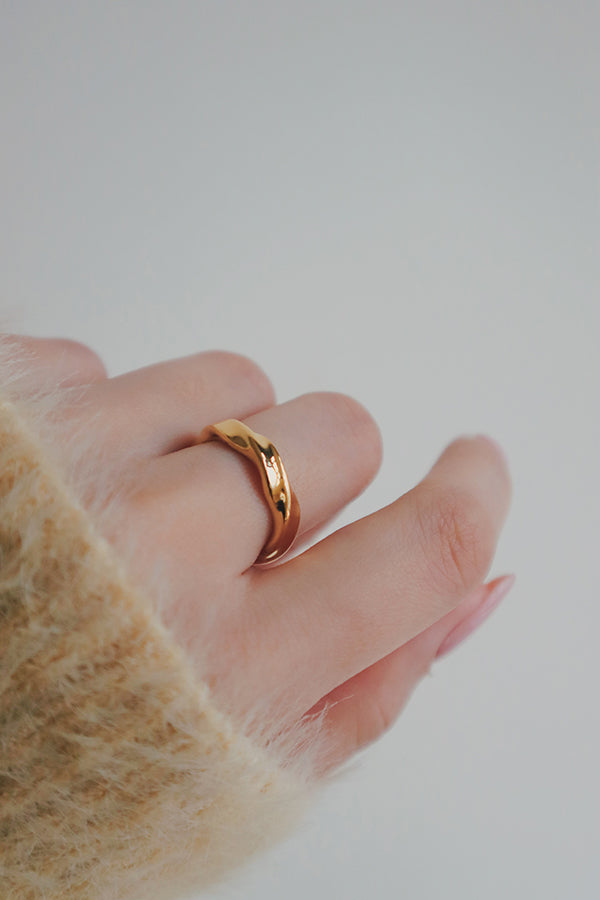 A detailed shot of a gold wave ring on a woman's hand. The ring features a unique wave pattern with a polished finish, creating a stylish and contemporary accessory that adds a subtle yet sophisticated touch to her look.