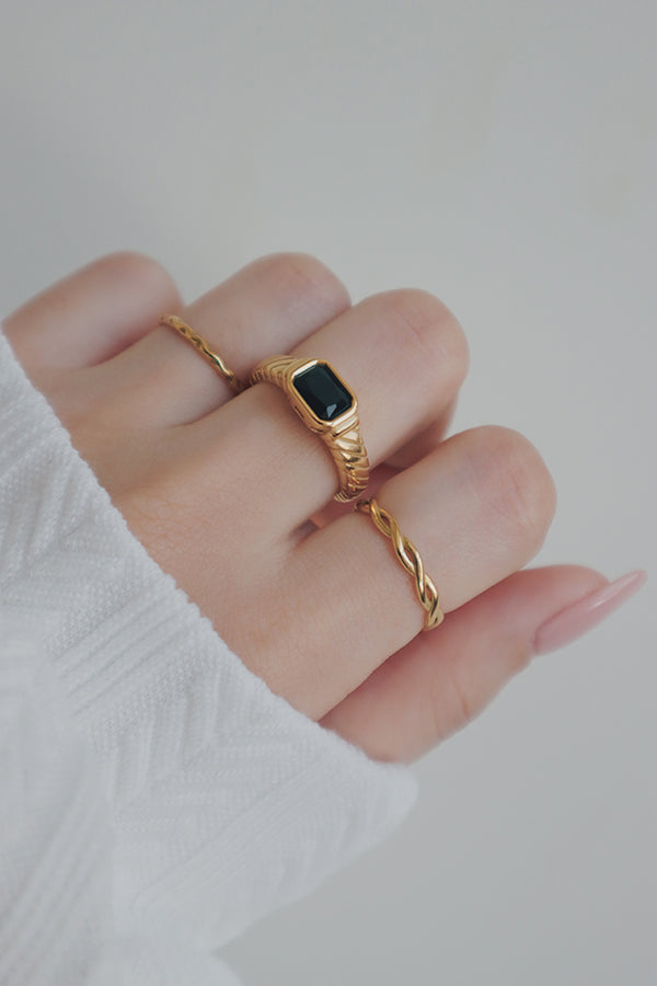 A close-up shot of a womans hand wearing a gold ring with a black cubic zirconia stone. The ring's rectangular stone and elegant band design create a bold and stylish look, perfect for mixing and matching with other jewelry pieces.