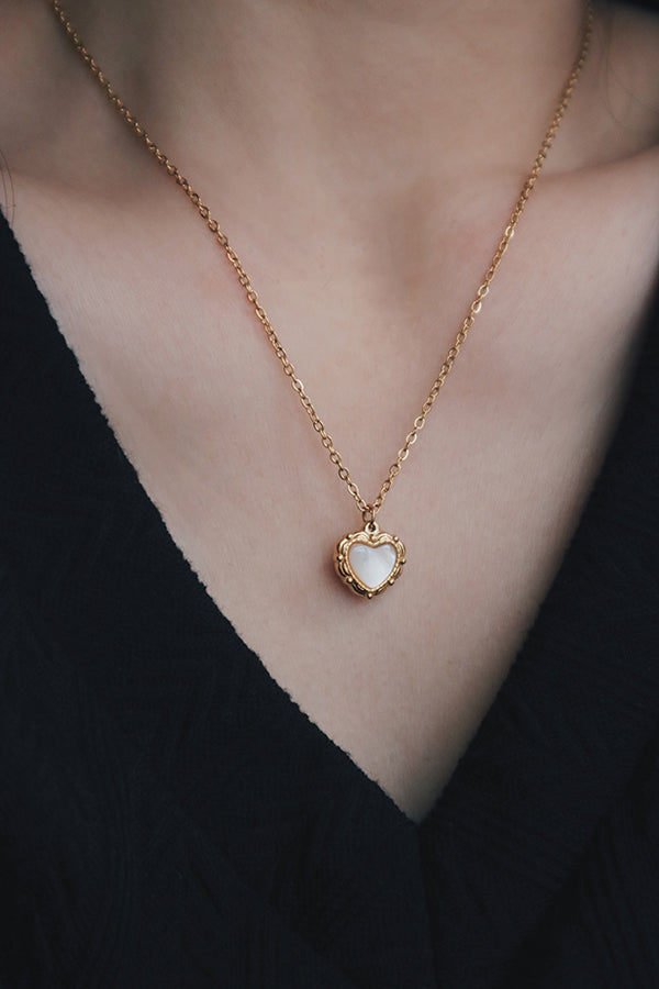 Product image of a heart-shaped pendant necklace with a mother-of-pearl inlay, displayed on a white background. The gold beaded frame and delicate chain are clearly visible.