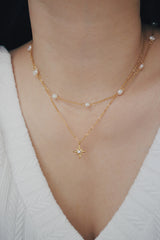 SH & Co. 18K gold Essie necklace with a pearl center, worn with a white top.