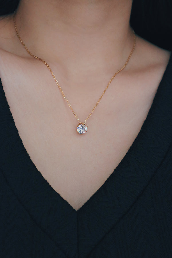 Close-up of a woman wearing an 18K gold-plated cubic zirconia solitaire necklace, styled with a black textured V-neck top, showcasing the necklace's brilliant round-cut stone.