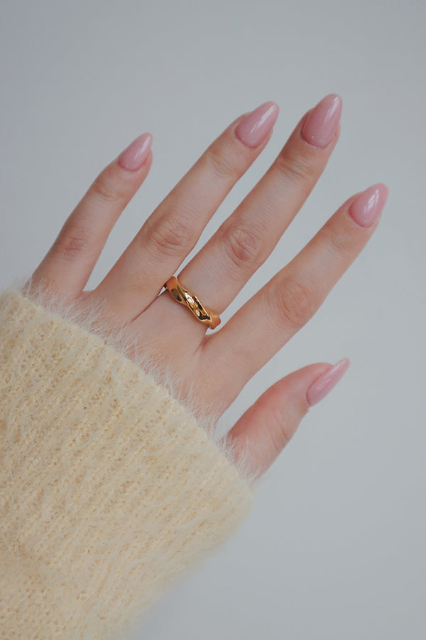 A close-up image of a womans hand adorned with a gold wave ring. The ring's smooth, flowing design mimics the shape of gentle waves, making it a versatile and fashionable piece for everyday wear.