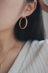 A close-up shot of a womans ear featuring a large, twisted texture gold hoop earring. The earrings unique texture and larger size make it a statement piece that can elevate any outfit.