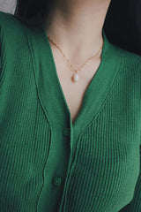 A woman wearing the SH & Co. freshwater pearl necklace with a gold-plated twisted chain, paired with a green knit cardigan, emphasizing the necklace's elegant design and craftsmanship.