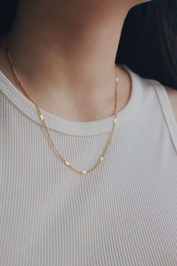 A woman wearing SH & Co. gold-plated necklace with delicate chain links, perfect for a subtle, elegant look.