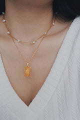 Elegant gold-plated necklace featuring a square pendant with a radiant sunburst pattern, accentuated by a multi-layered chain with delicate freshwater pearls, perfect for a sophisticated look.