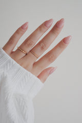 A close-up image of a womans hand adorned with a slim gold ring. The ring's slender band and subtle wave detail offer a refined and understated look, perfect for adding a touch of elegance to any outfit.