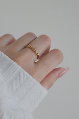 A close-up shot of a womans hand adorned with a gold woven ring. The ring's delicate, braided design adds a touch of elegance and sophistication, making it an ideal piece for both casual and formal occasions.