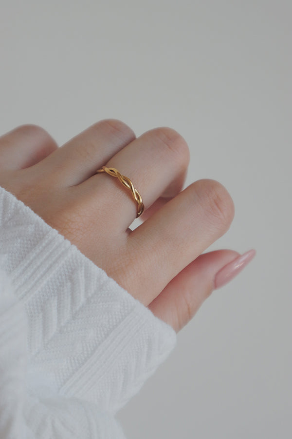 A close-up shot of a womans hand adorned with a gold woven ring. The ring's delicate, braided design adds a touch of elegance and sophistication, making it an ideal piece for both casual and formal occasions.