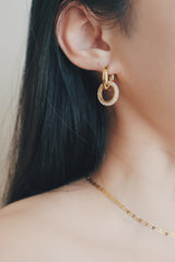 A detailed image of a woman’s ear adorned with gold hoop earrings that include a dangling charm covered in sparkling cubic zirconia stones. The earrings are designed to catch the light, adding a touch of glamour and sophistication to any outfit.