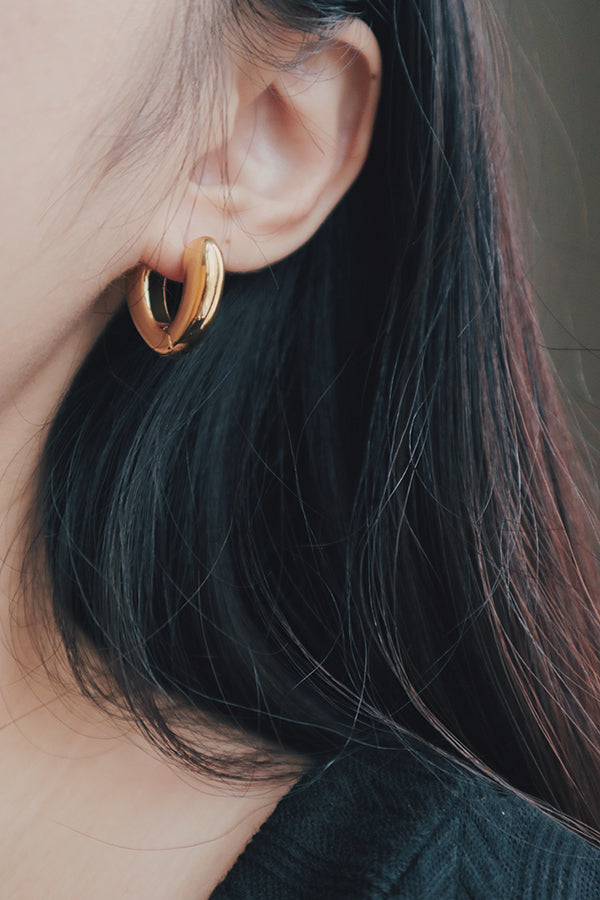 A detailed image of a woman wearing gold heart-shaped hoop earrings. The earrings are heart-shaped with a smooth, shiny finish that reflects light beautifully, making them a stylish addition to her jewelry collection.