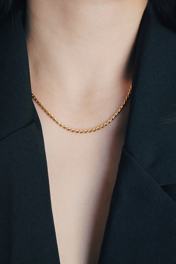 Close-up of a 18K gold-plated rope chain necklace styled on a woman wearing a black blazer, focusing on the chain's detailed twist design and elegant drape.