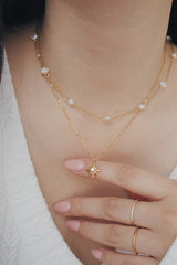 SH & Co. star necklace with a pearl center, worn with a green knit top.