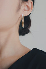 A close-up shot of a womans ear featuring tassel earrings made of gold and cubic zirconia. The earrings' long, dangling design adds movement and sparkle, creating a dramatic yet elegant accessory.