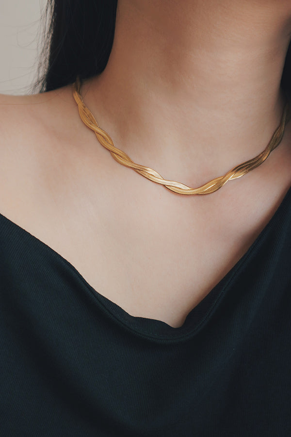 A woman wearing a statement herringbone gold necklace that sits elegantly along her collarbone, paired with a dark blouse.