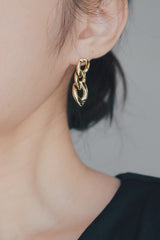 A close-up image of a woman's ear adorned with Cuban chain gold earrings. The earrings have a distinctive design of interconnected gold links that dangle elegantly, making them a fashionable accessory that adds a modern edge to any outfit.