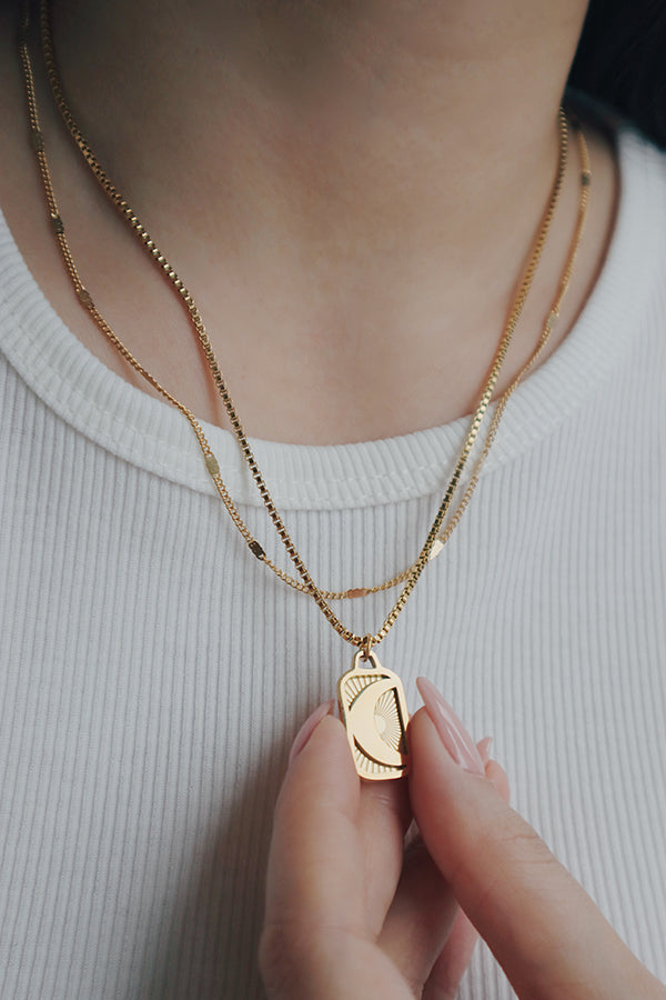 A woman wearing a layered necklace set featuring the Phoebe Luna necklace with a crescent moon and sunburst design, styled with a white ribbed top, creating a chic and modern look.