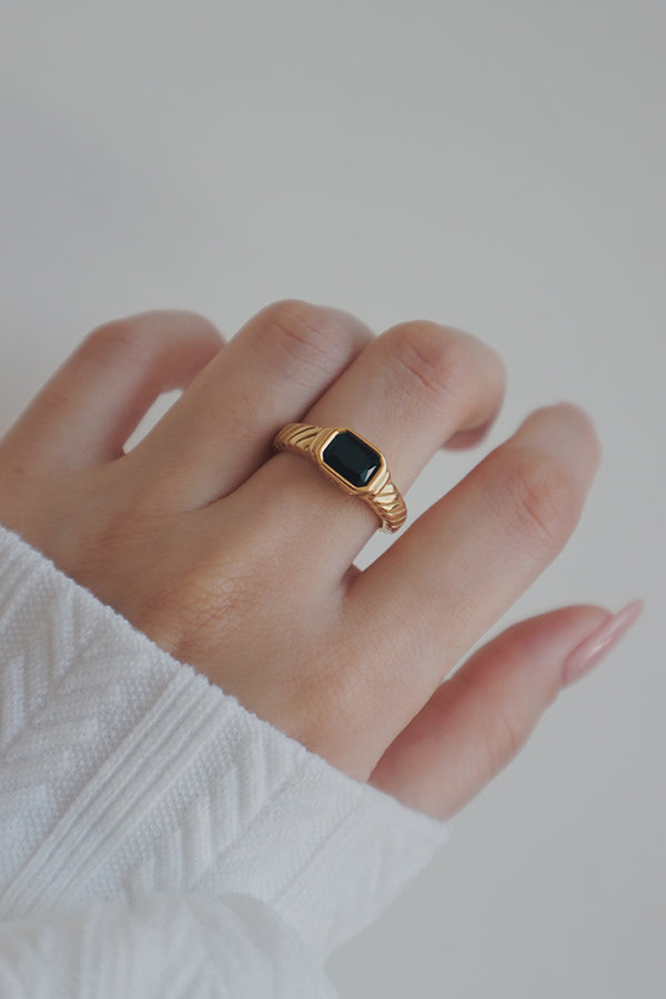 A close-up image of a womans hand showcasing a tarnish-free gold ring with a black cubic zirconia stone. The rings stylish design and high-quality finish make it an excellent choice for everyday wear or special occasions.