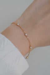 A tarnish-free gold bracelet with cubic zirconia stones evenly spaced along the chain, worn on the wrist with a white textured sleeve.