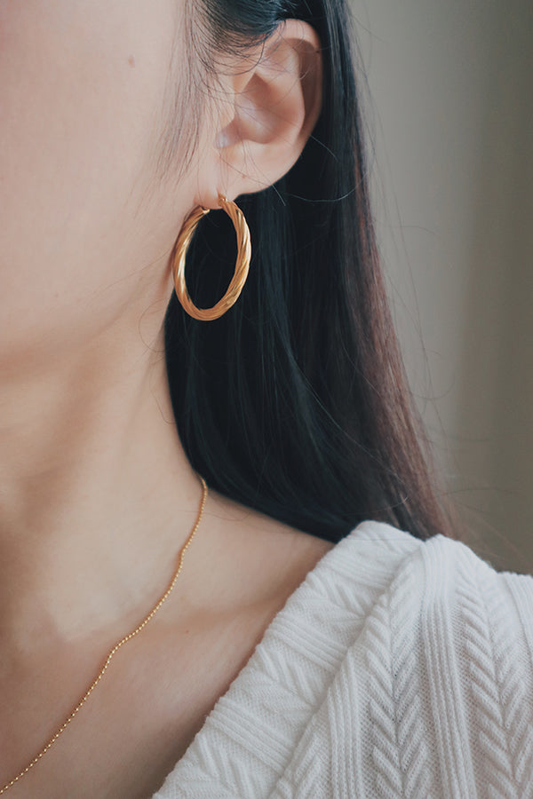 A close-up image showing a woman wearing a larger version of the twisted texture gold hoop earring. The earring has a bold, yet elegant design, with the twisted texture adding a touch of sophistication to the overall look.