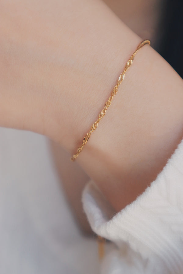 Delicate gold Singapore chain bracelet on a woman's wrist, displaying its intricate twisted design and adjustable clasp for a perfect fit.