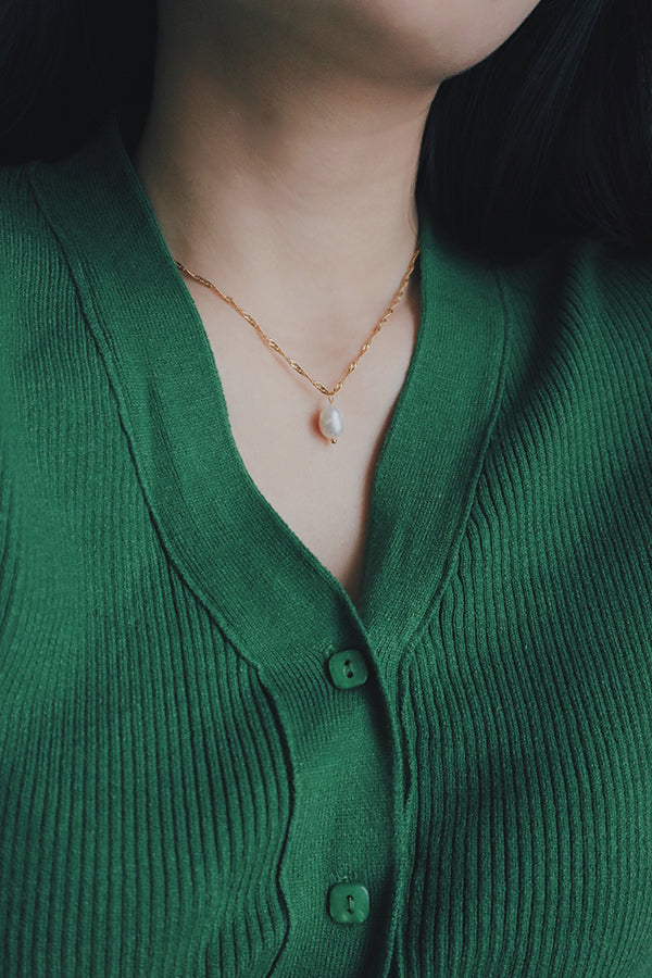 Close-up of a woman wearing a tarnish-free hypoallergenic gold necklace with a single freshwater pearl pendant, styled with a green knit top, highlighting the necklace's delicate and versatile style.