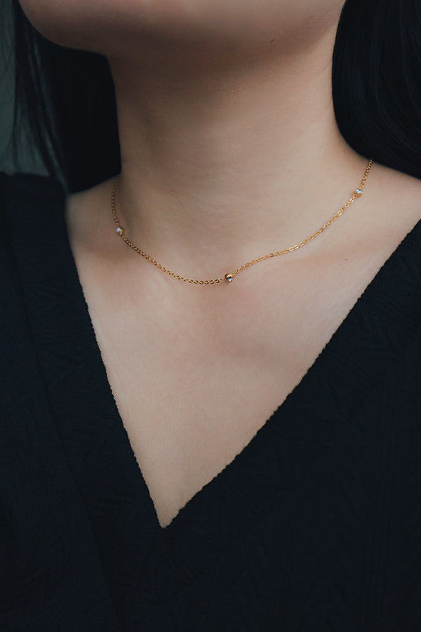 Close-up view of a minimalist gold necklace with evenly spaced cubic zirconia stones, styled as a choker with a black V-neck top.