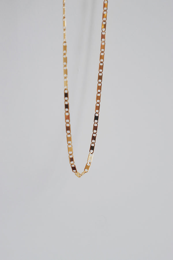 Simple and elegant gold choker with a piggy snout-inspired design, hanging against a plain white background for a clear view.