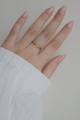 A close-up image of a womans hand showcasing a gold woven ring. The ring's twisted, woven pattern creates a unique and trendy appearance, making it a perfect accessory for stacking or wearing on its own.