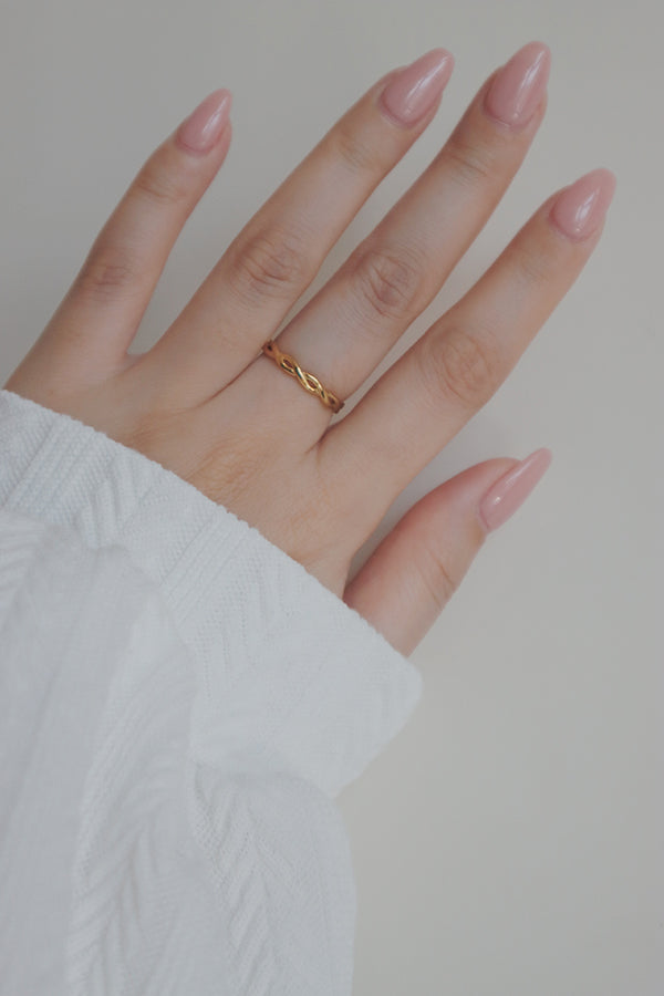 A close-up image of a womans hand showcasing a gold woven ring. The ring's twisted, woven pattern creates a unique and trendy appearance, making it a perfect accessory for stacking or wearing on its own.