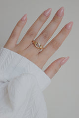 A close-up image of a gold ring featuring a clear cubic zirconia stone set in a rectangular frame. The rings refined design, with its detailed band and sparkling stone, is perfect for adding a touch of sophistication to any outfit.